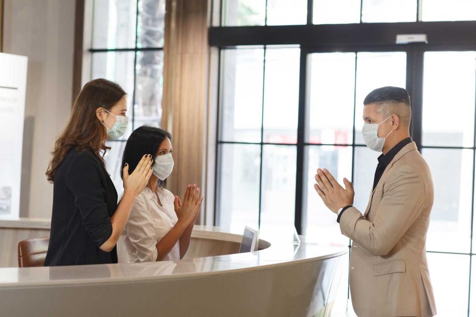 Hotel guest and receptionist wearing mask to protect from conronavirus covid-19 having new practice of greeting with Thai Wai