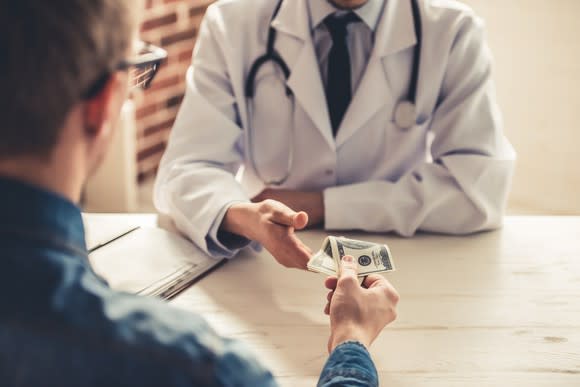 A man handing cash to a doctor behind a desk.