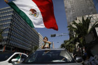 An anti-government demonstrator waves a Mexican flag as he rides out the sunroof of a car during a driving protest by hundreds of cars, calling for the resignation of President Andres Manuel Lopez Obrador, in Mexico City, Sunday, June 28, 2020. (AP Photo/Rebecca Blackwell)