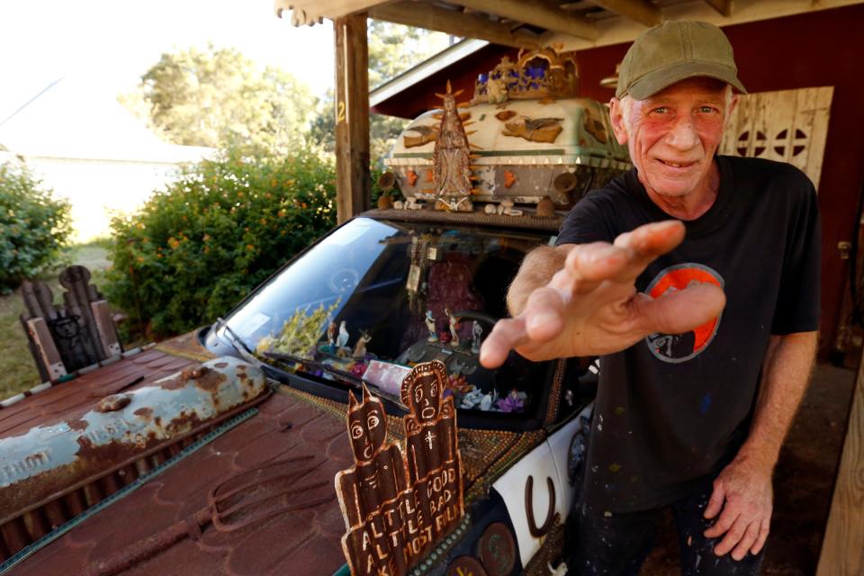 Folk artist Chris Hubbard's poses for a photo with his Heaven and Hell art car at his home in Farmington, Ga., on Wednesday, Oct. 5, 2022. Hubbard's pose with his hand raises is a tribute to one of his mentors folk artist Howard Finster.