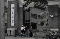 A woman shows a security guard proof for entry near the words "Peking University" at one of the entrance to the main campus of Peking University on Tuesday, May 17, 2022, in Beijing. Administrators at the elite Beijing university have backed down from plans to further tighten pandemic restrictions on students as part of China’s “zero-COVID” strategy after a weekend protest at the school, according to students Tuesday. (AP Photo/Ng Han Guan)