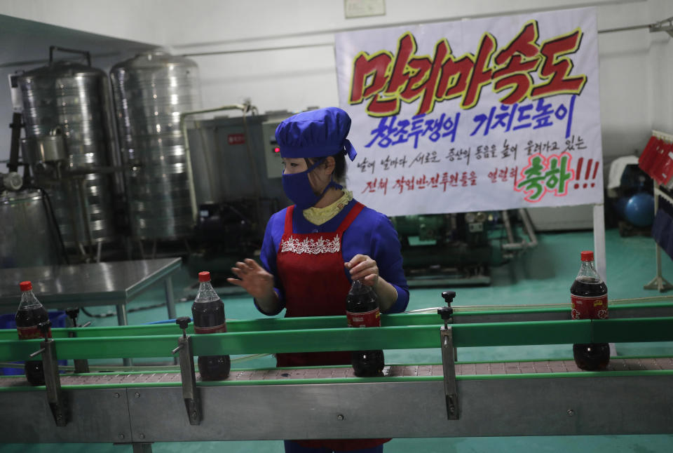 In this March 13, 2019, photo, a worker runs a conveyor belt moving bottles of soft drinks near a propaganda banner that reads "Let's uphold the banner of the speed of Mallima (a mythical Pegasus-type horse)" at Kumkhop Trading Co. food factory in Pyongyang, North Korea. North Korean factories are filling city store shelves with ever better and fancier snack foods and sugary drinks, while government officials and international aid organizations warn the nation could be on the verge of a major food crisis. (AP Photo/Dita Alangkara)