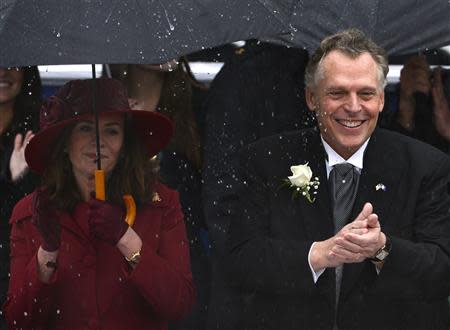 Terry McAuliffe (R) applauds in the heavy rain as his wife Dorothy holds an umbrella as they arrive for his swearing-in ceremony as Virginia's governor, in Richmond, Virginia, January 11, 2014. REUTERS/Mike Theiler