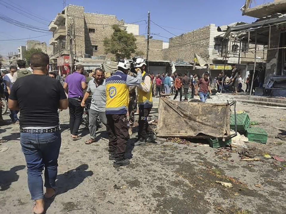 This photo provided by the Syrian Civil Defense White Helmets, which has been authenticated based on its contents and other AP reporting, shows a Syrian White Helmet civil defense workers, center, gather with civilians at the rocket attacked scene, at al-Bab town, north Syria, Friday, Aug. 19, 2022. A rocket attack on a crowded market in a town held by Turkey-backed opposition fighters in northern Syria Friday killed several people and wounded dozens, an opposition war monitor and a paramedic group reported. (Syrian Civil Defense White Helmets via AP)