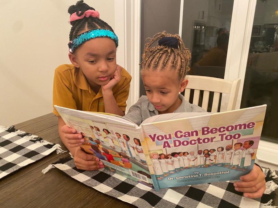 Second grader Skylar Tolbert, 7, peers over the shoulder of her younger sister, Sydney, 6, a kindergartner at Libertas School of Memphis. The sisters read at home each night after school.