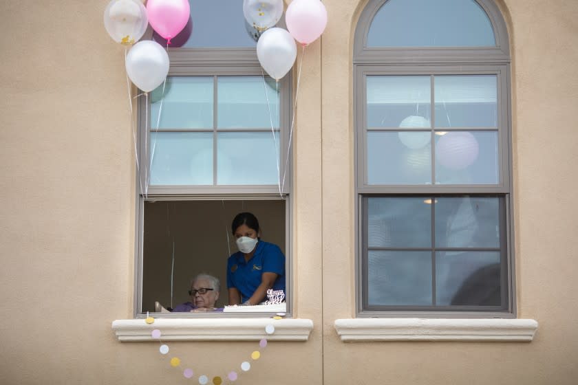 REDONDO BEACH, CA --APRIL 07, 2020 -Margaret Jones, assisted by Kensington employees, waves from her second-story window, to Amber and Lucy Cavazos, from Huntington Park, who had used a lift to help celebrate Jones' 91st birthday, in the courtyard of the assisted living facility, in Redondo Beach, CA, during the coronavirus pandemic April 07, 2020. Lucy Cavazos has celebrated Jones' birthday with her for 20 year and Amber considers her to be a grandmother. The two didn't want to let the coronavirus pandemic break their tradition. (Jay L. Clendenin / Los Angeles Times)