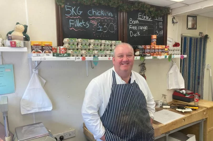 Jason Parr, owner of J&K Parr Butchers in Sutton, wearing a black and white striped apron behind his shop counter