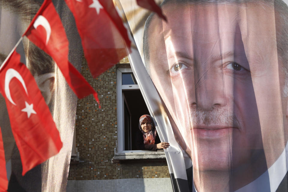 File- In this Tuesday, March 5, 2019 file photo, a woman peers out of her window behind a banner of Turkey's President Recep Tayyip Erdogan, following Erdogan speech at a rally of his ruling Justice and Development Party's (AKP) in Istanbul, ahead of local elections scheduled for March 31, 2019. Erdogan has been holding multiple daily rallies across the country, using highly polarising language, portraying the opposition as traitors who are supported by terrorists, blaming ills on foreign forces and stirring up nationalist and religious sentiments. (AP Photo/Lefteris Pitarakis, File)