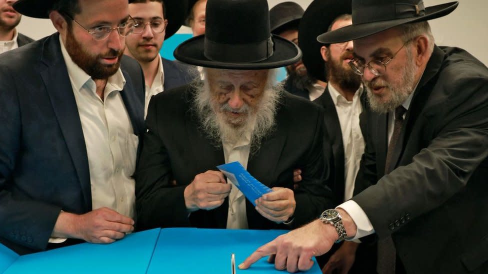 Un grupo de judíos ortodoxos le ayuda a un anciano de la comunidad a depositar su voto en las elecciones legislativas.