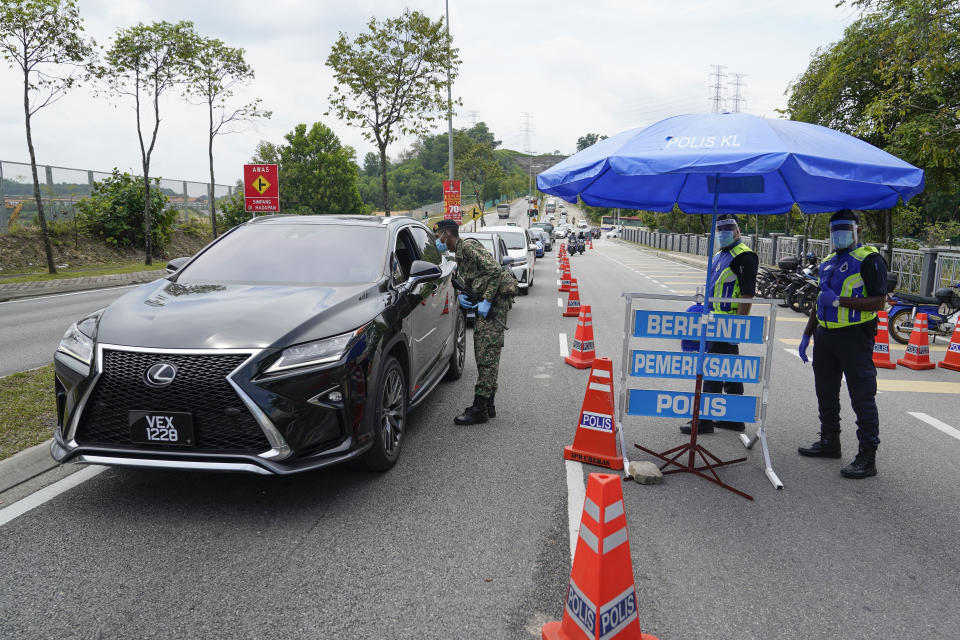 Police officers check vehicles at roadblock to ensure that people abide by the movement control order on the outskirts of Kuala Lumpur, Malaysia, Wednesday, Oct. 14, 2020. Malaysia will restrict movements in its biggest city Kuala Lumpur, neighboring Selangor state and the administrative capital of Putrajaya from Wednesday to curb a sharp rise in coronavirus cases. (AP Photo/Vincent Thian)