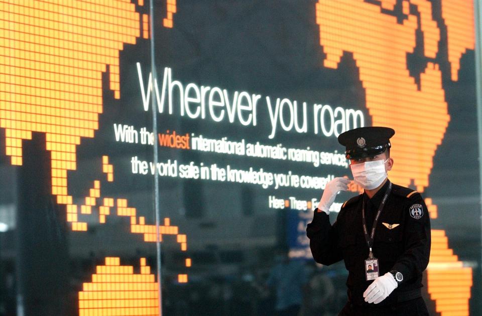 An airport guard wears a surgical mask to protect himself from severe acute respiratory syndrome, or SARS, as he walks past an advertisement featuring a world map and a slogan that reads: 