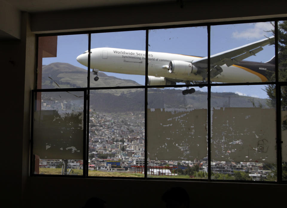 In this Jan. 8, 2013 photo, a plane approaches the Mariscal Sucre airport for landing, seen through a glass wall inside the Eloy Alfaro school in Quito, Ecuador. Landing at Ecuador’s capital can be a white-knuckle affair. High altitude, a cramped runway and towering, active volcanos nearby make it one of Latin America’s most challenging aiports for pilots. And the constant roar of the planes has tormented those on the ground as well. Mariscal Sucre airport sat amid cornfields when it was christened in 1960, and on Feb. 19, the airport will close and a new airport will be built in an agricultural setting 12 miles (20 kilometers) northeast of the capital. (AP Photo/Dolores Ochoa)