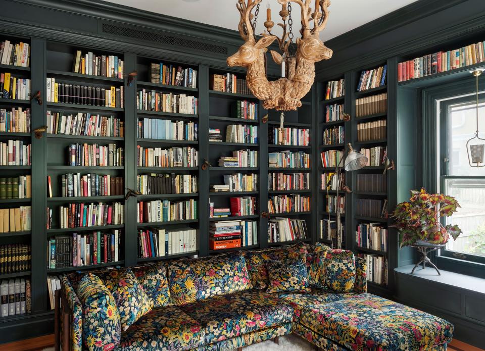 Painted in Studio Green by Farrow & Ball, the library reads as a magical forest of sorts, with a vintage chandelier in the form of three stags, a menagerie of carved birds gathered on the bookshelves, and a Neri&Hu sectional upholstered in exuberant botanical fabric.