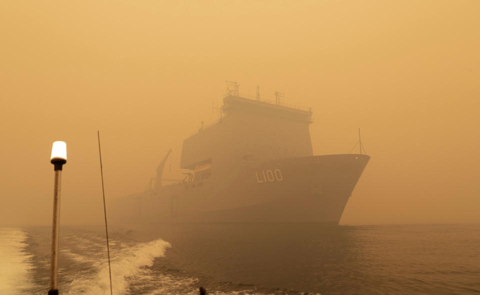 In this photo released and taken Jan. 2, 2020, by the Australian Department of Defense, the HMAS Choules sails off the coast of Mallacoota, Victoria to supply support to people cut off by bush fires. Navy ships plucked hundreds of people from beaches and tens of thousands were urged to flee before hot weather and strong winds in the forecast worsen Australia's already-devastating wildfires. (Australian Department of Defense via AP)