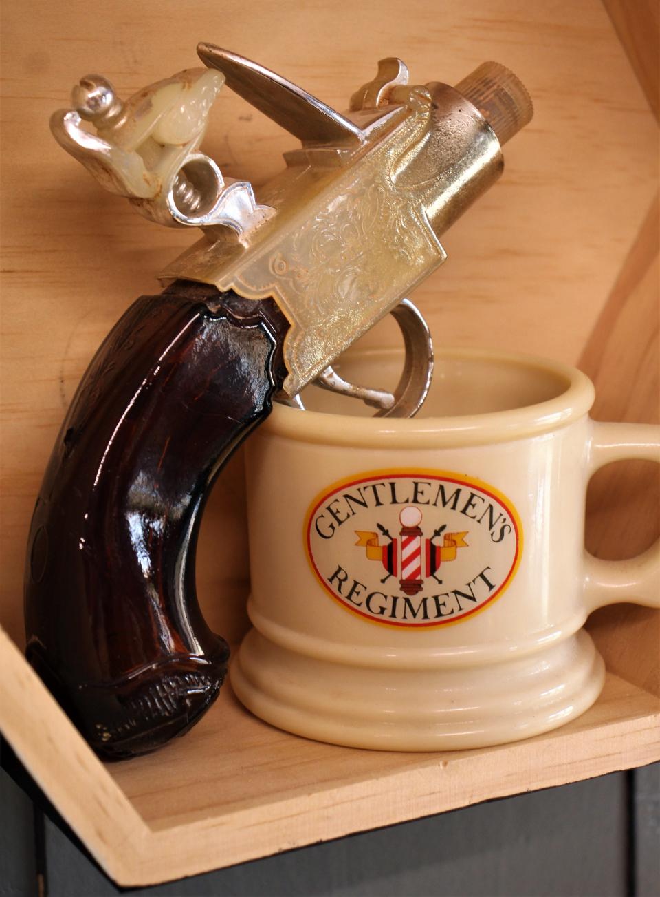 A pistol-shaped bottle of cologne next to a shaving cream cup.