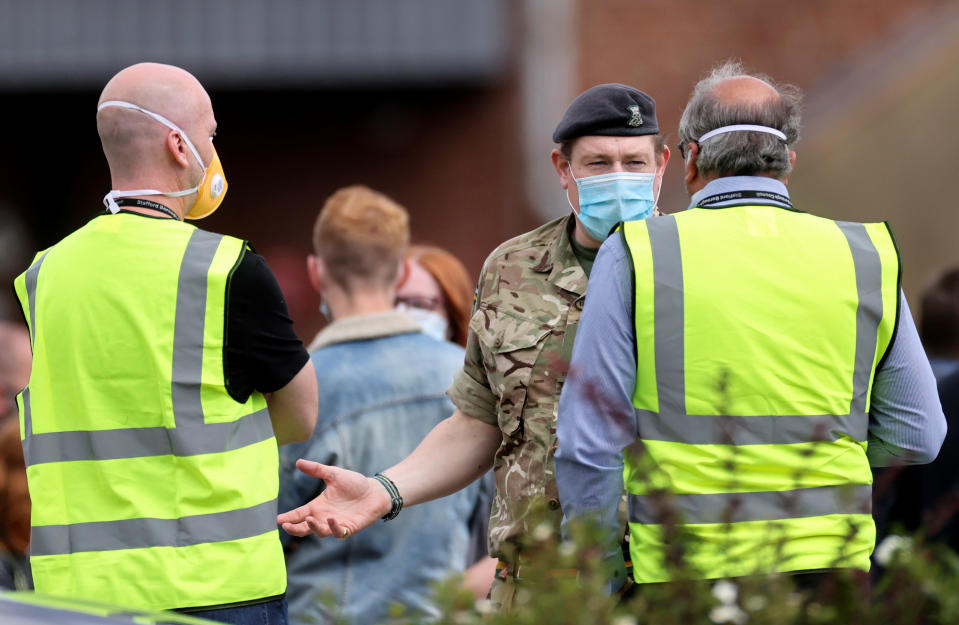 A soldier wearing a face mask gestures as people queue near the Crown and Anchor pub following a spike in cases of the coronavirus disease (COVID-19) to visitors of the pub in Stone, Britain, July 29, 2020. REUTERS/Carl Recine