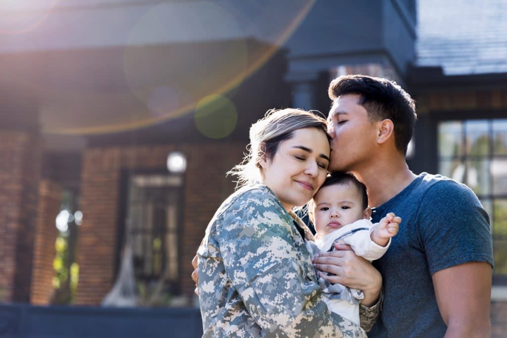 A couple with a veteran mother pose for a portrait outside of a home. Veterans Affairs offer the best mortgage insurance for veterans.