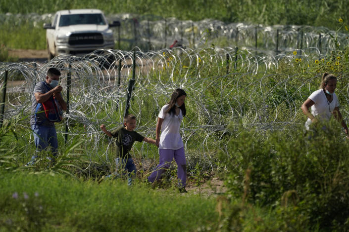 Migrants walk along concertina wire toward Border Patrol officers after illegally crossing the Rio Grande from Mexico into the U.S. at Eagle Pass, Texas, Friday, Aug. 26, 2022. The area has become entangled in a turf war between the Biden administration and Texas Gov. Greg Abbott over how to police the U.S. border with Mexico. (AP Photo/Eric Gay)