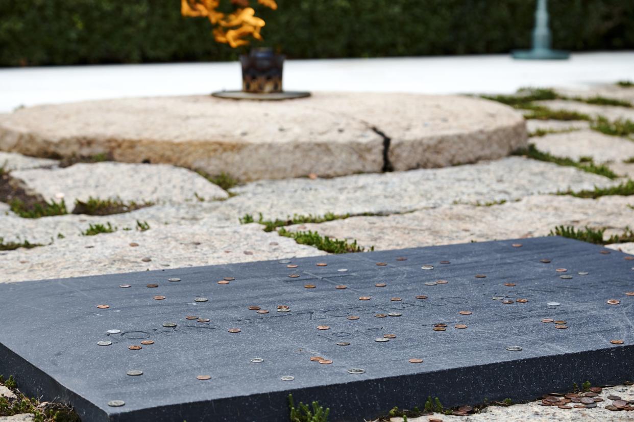 Closeup of President John F. Kennedy's grave, Arlington, Virginia, several coins on a dark headstone with the eternal flame in the background