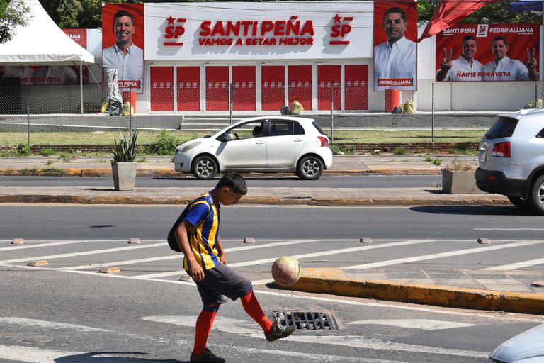 Un chico juega al fútbol delante de un local partidario del precandidato del Partido Colorado, Santiago Peña