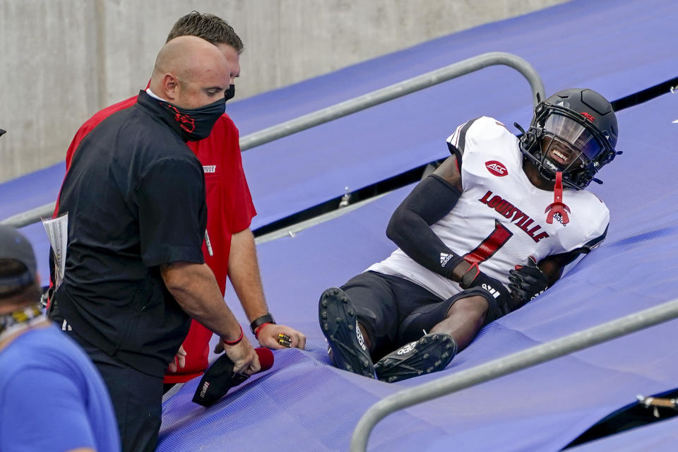 Trainers tend to Louisville running back Javian Hawkins (10) as he lies on a tarp after he tumbled across the tarps covering seats behind the end zone after dropping a pass during the second half of an NCAA college football game against Pittsburgh, Saturday, Sept. 26, 2020, in Pittsburgh. Pittsburgh won 23-20. (AP Photo/Keith Srakocic)