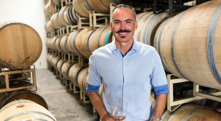 The owner of a small winery, standing in front of a row of oak barrels