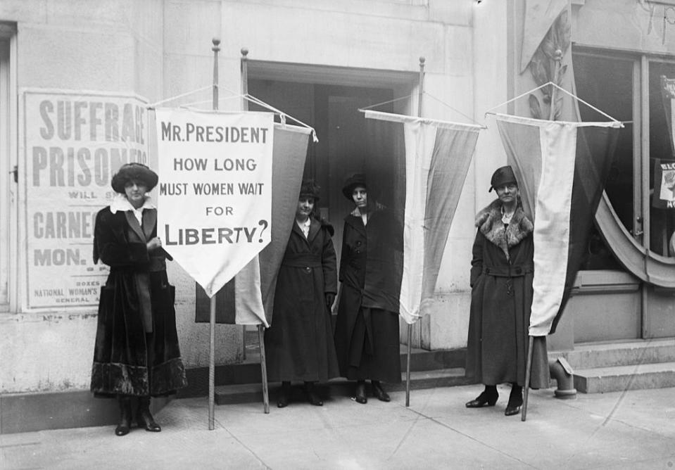 Women suffragists hold banners questioning the President about women's liberty next to a building