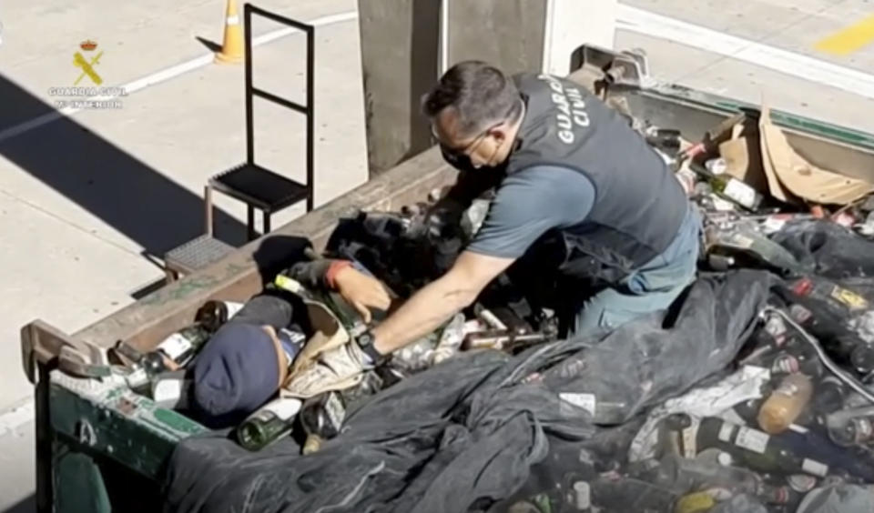 In this image taken from video made available by the Guardia Civil, an officer of the Guardia Civil helps a man out from under glass bottles in a container in Melilla, Spain, Friday Feb. 19, 2021. Spanish authorities say they have found and rescued 41 migrants who tried to reach continental Europe from North Africa in the past four days, some of them hiding inside a container of discarded glass bottles and a bag of toxic ash. (Guardia Civil via AP)