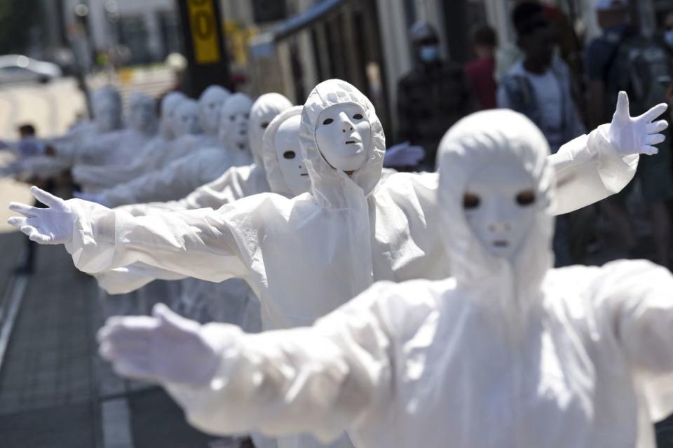 Performers, wearing a white mask and a protective outfit gesture during a demonstration against the new coronavirus safety measures including a compulsory health pass. Source: Getty