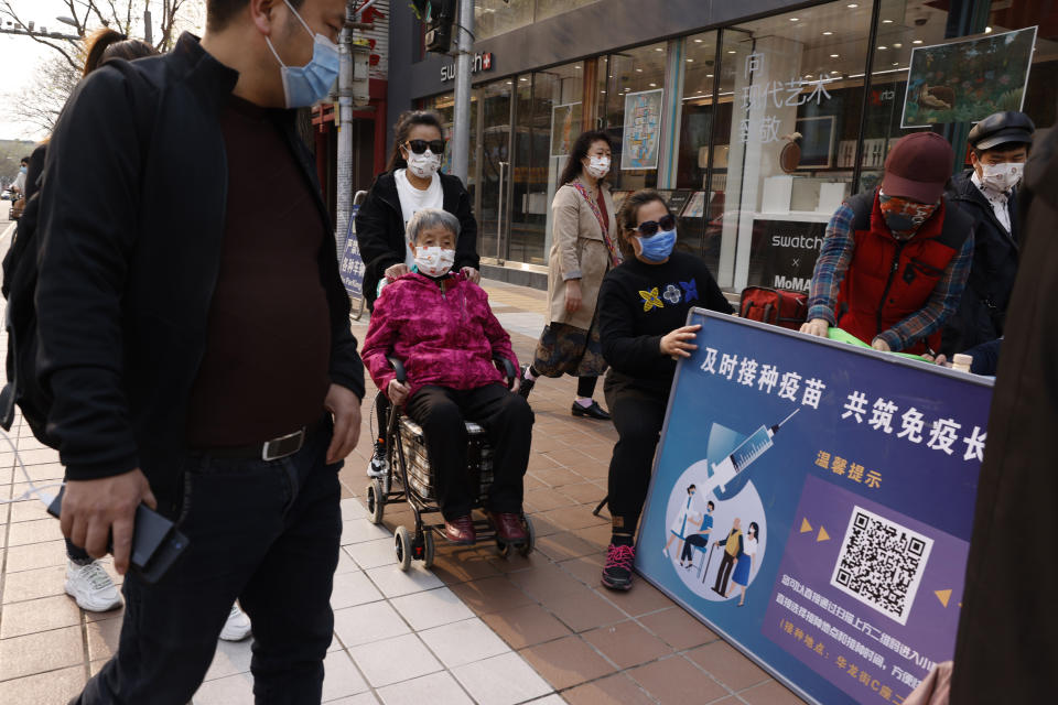 A woman in a wheel chair is pushed past a stand promoting Chinese coronavirus vaccines in Beijing Friday, April 9, 2021. In a rare admission of the weakness of Chinese coronavirus vaccines, the country's top disease control official says their effectiveness is low and the government is considering mixing them to give them a boost. (AP Photo/Ng Han Guan)