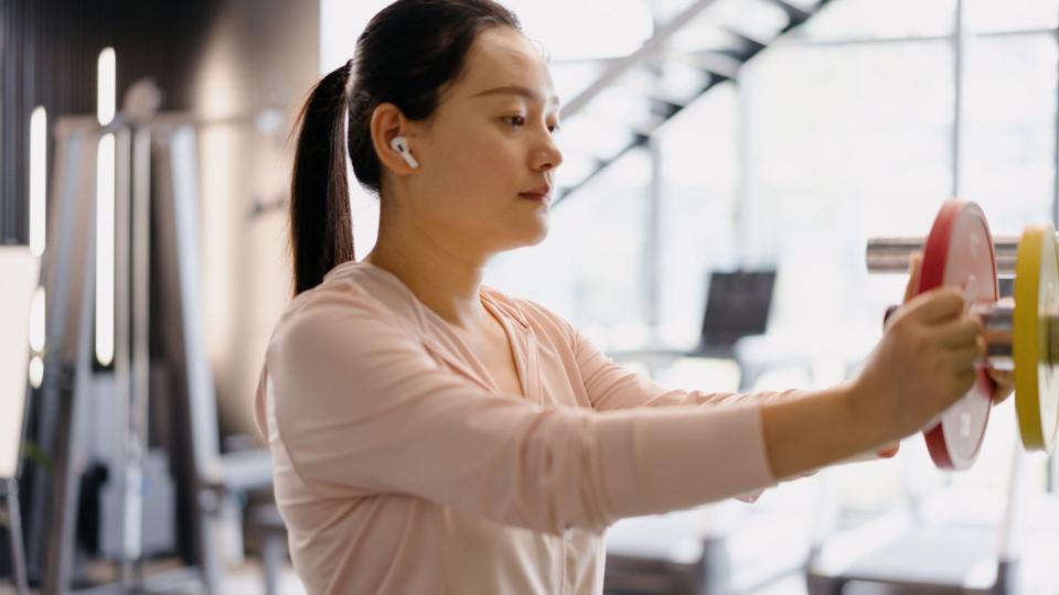 Woman racking barbell with small weights, wearing headphones