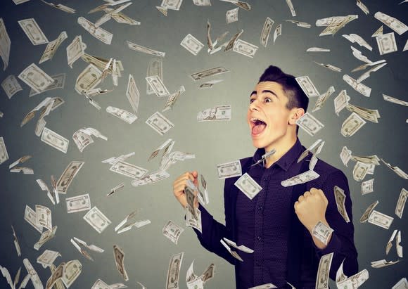 A smiling young man stands in a shower of paper currency