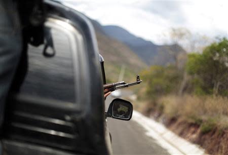 A vigilante aims his weapon out of a car window while driving in a convoy with others to Poturo December 29, 2013. REUTERS/Jorge Dan Lopez/Files