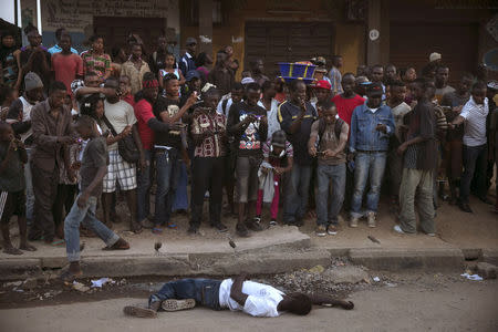 Bystanders stand around the body of a suspected Ebola victim lying in a street in the town of Koidu, Kono district in Eastern Sierra Leone, December 18, 2014. REUTERS/Baz Ratner