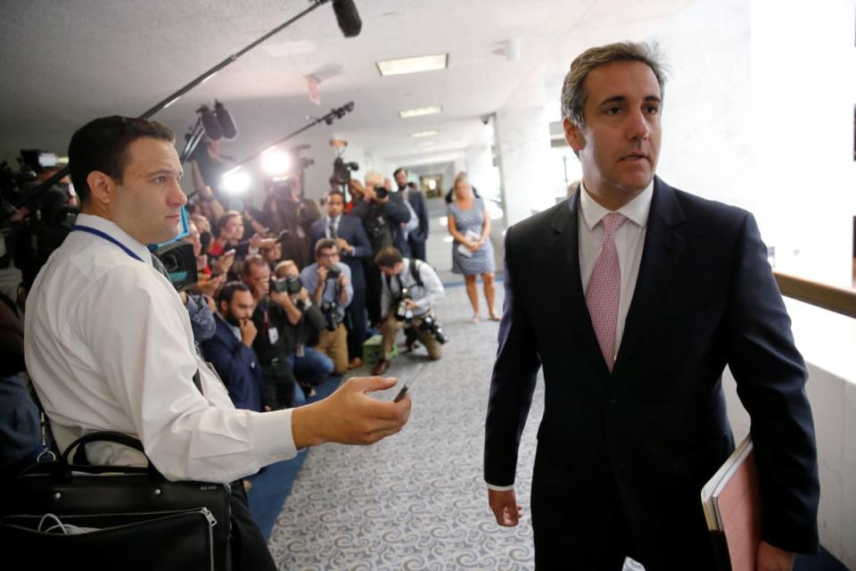Michael Cohen, wearing a suit, walks by dozens of reporters at the U.S. Capitol.