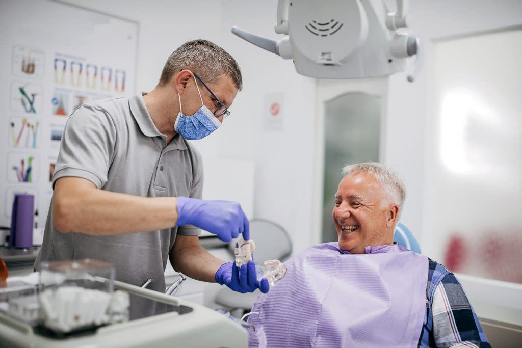 A senior citizen laughs as a dentist shows him dentures. 