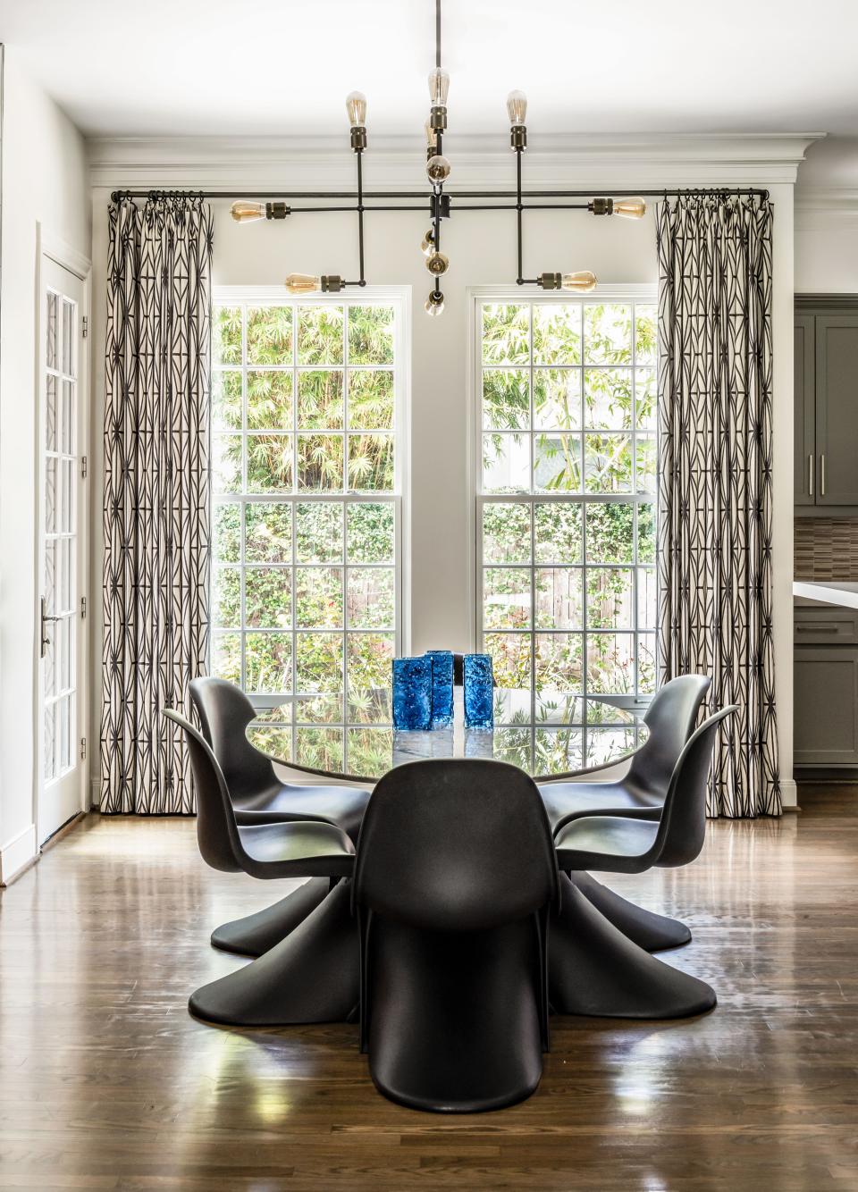 Set off the family room and kitchen, the breakfast area features a classic midcentury table by Room & Board, era-appropriate molded plastic chairs by Design Within Reach, and lighting from Wayfair. The curtains pop in every room; here they are made with a Kelly Wearstler fabric.