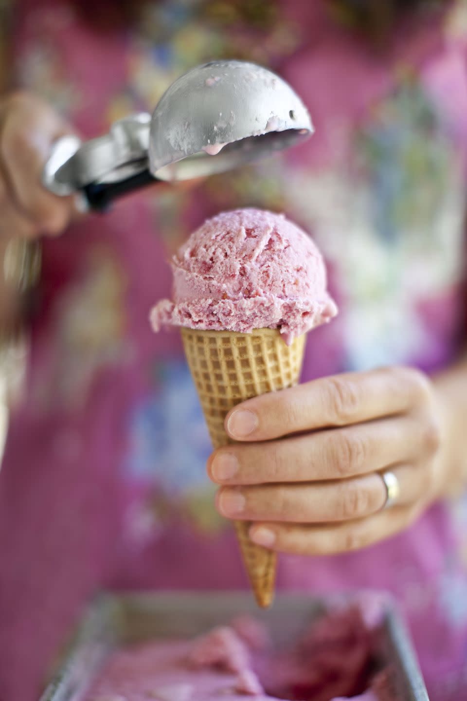 a woman adding a scoop of raspberry cheesecake ice cream to an ice cream cone