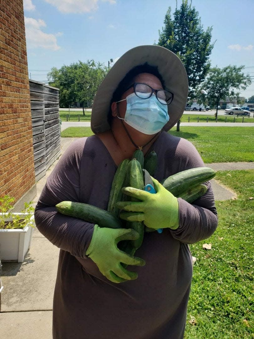 LeTicia Marshall, with her hands full of cucumbers, stands outside the now-defunct community garden outside the Shively-Newman Library, July 27, 2021.