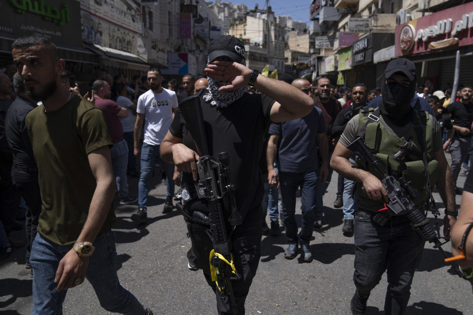 A Palestinian militant from the Lions' Den group covers his face at the sight of a camera while taking part in the funeral procession of three comrades who were killed by Israeli forces, Hassan Qatnani, Moaz al-Masri and Ibrahim Jabr, in the West Bank city of Nablus, Thursday, May 4, 2023. The killing of Zuhair al-Ghaleeth last month, the first slaying of a suspected Israeli intelligence collaborator in the West Bank in nearly two decades, has laid bare the weakness of the Palestinian Authority and the strains that a recent surge in violence with Israel is beginning to exert within Palestinian communities. (AP Photo/Nasser Nasser)