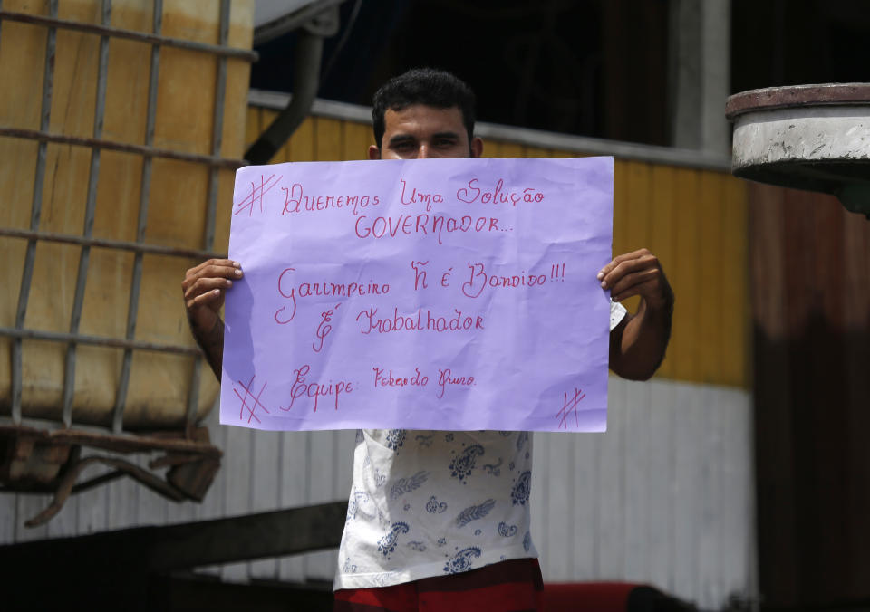 An illegal gold miner holds a sign that reads in Portuguese "Governor, we want a solution. A Garimpeiro is not a criminal, but a worker. Golden Fever Team," at a dredging barge on the Madeira river, a tributary of the Amazon river in Autazes, Amazonas state, Brazil, Thursday, Nov.25, 2021. Hundreds of mining barges have arrived during the past two weeks after rumors of gold spread, with environmentalists sounding the alarm about the unprecedented convergence of boats in the sensitive ecosystem. (AP Photo/Edmar Barros)