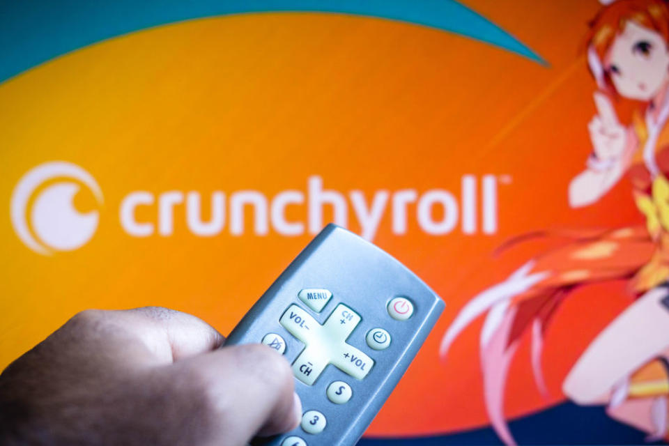 BRAZIL - 2021/06/03: In this photo illustration a close-up of a hand holding a TV remote seen displayed in front of Crunchyroll logo. (Photo Illustration by Rafael Henrique/SOPA Images/LightRocket via Getty Images)