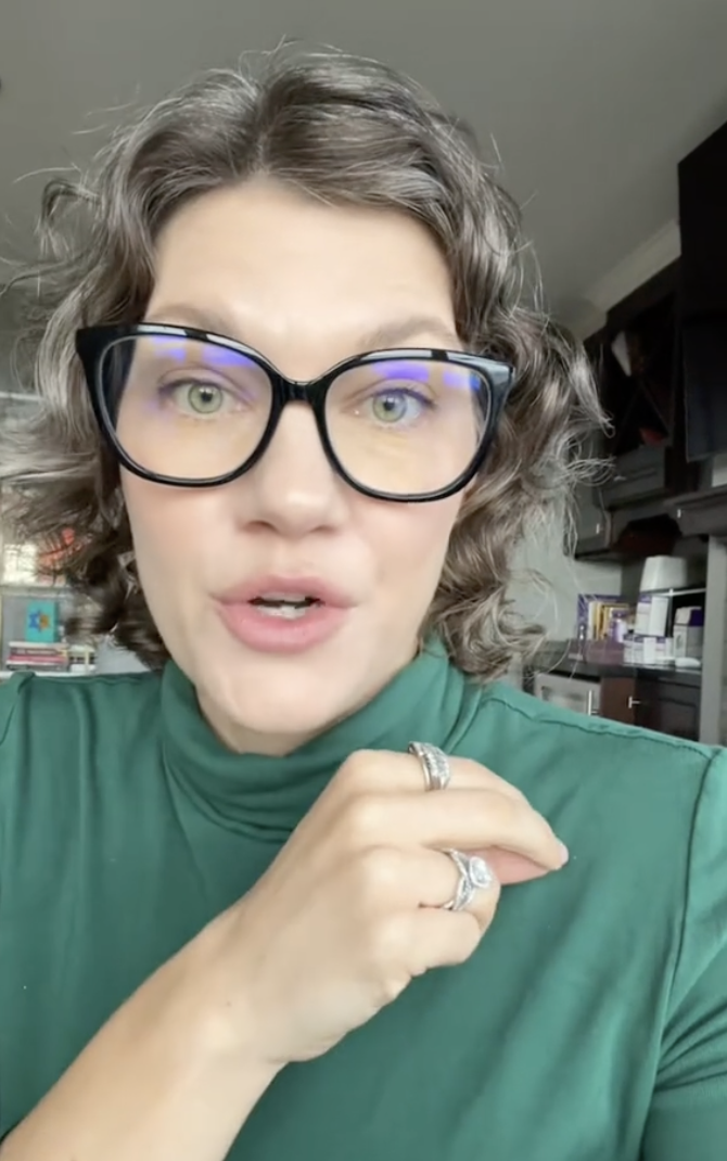 Woman in glasses with hand gesture, wearing a high-neck top, in an indoor setting