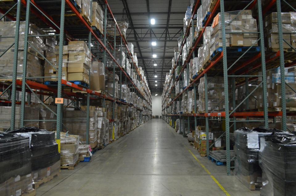 A long row of boxes sit on four layers of shelves inside a warehouse.
