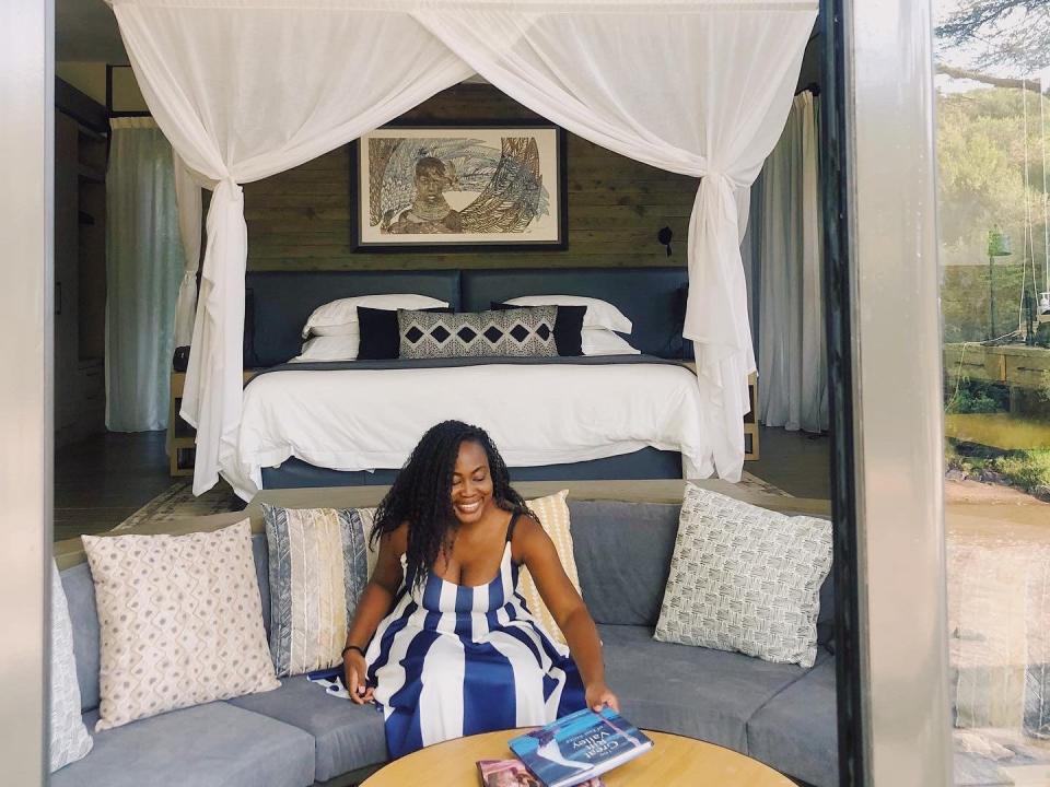 A woman sitting on a couch in front of a canopied bed.