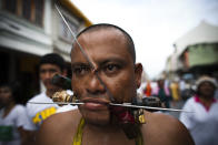 PHUKET, THAILAND - OCTOBER 04: A devotee of the Chinese shrine of Kathu Shrine, pierces his cheeks with skewers during a procession of Vegetarian Festival on October 4, 2011 in Phuket, Thailand. Ritual Vegetarianism in Phuket Island traces it roots back to the early 1800's. The festival begins on the first evening of the ninth lunar month and lasts for nine days. Participants in the festival perform acts of body piercing as a means of shifting evil spirits from individuals onto themselves and bring the community good luck. (Photo by Athit Perawongmetha/Getty Images)