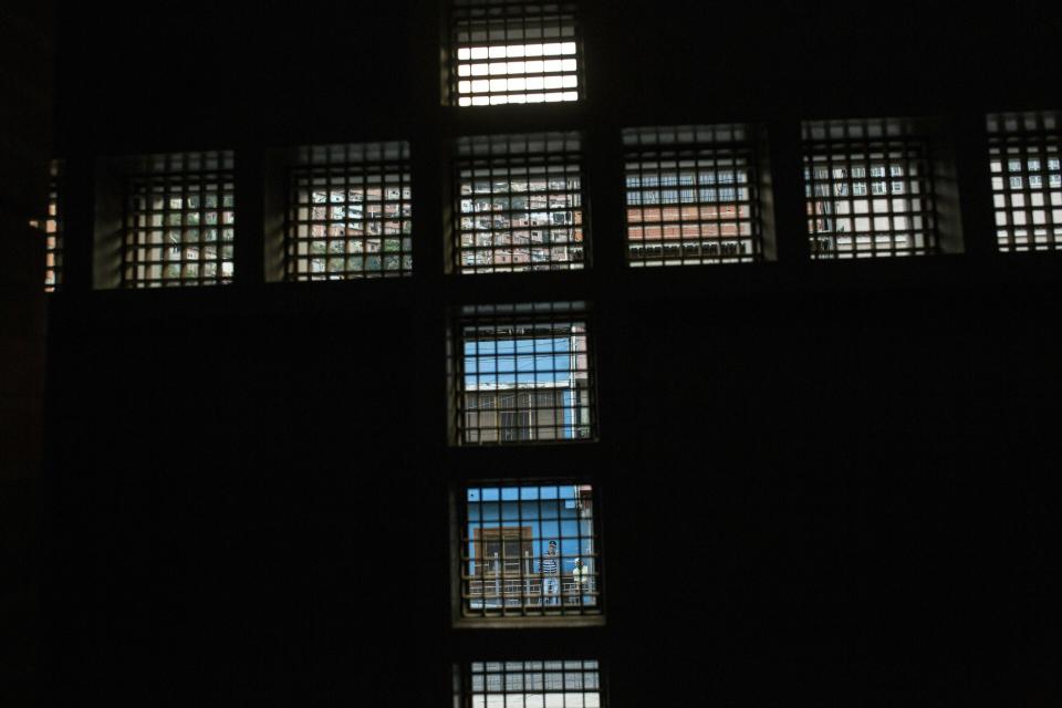 Residents can be seen though holes that form the shape of a cross, photographed from inside the Nazareno church where people pray for Nick Samuel Oropeza who was killed when anti-government protests broke out the previous week, in Caracas, Venezuela, Monday, Jan. 28, 2019. The 19-year-old's family says he was last seen alive on Jan. 23 fleeing alongside other anti-government protesters through Las Adjuntas slum as national guardsmen opened fire on people who had blocked streets with mounds of trash. (AP Photo/Rodrigo Abd)