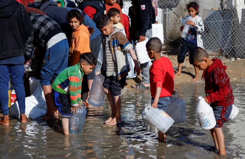 拉法市湧入流離失所的民眾，孩童18日在難民營拿桶子領水。路透社