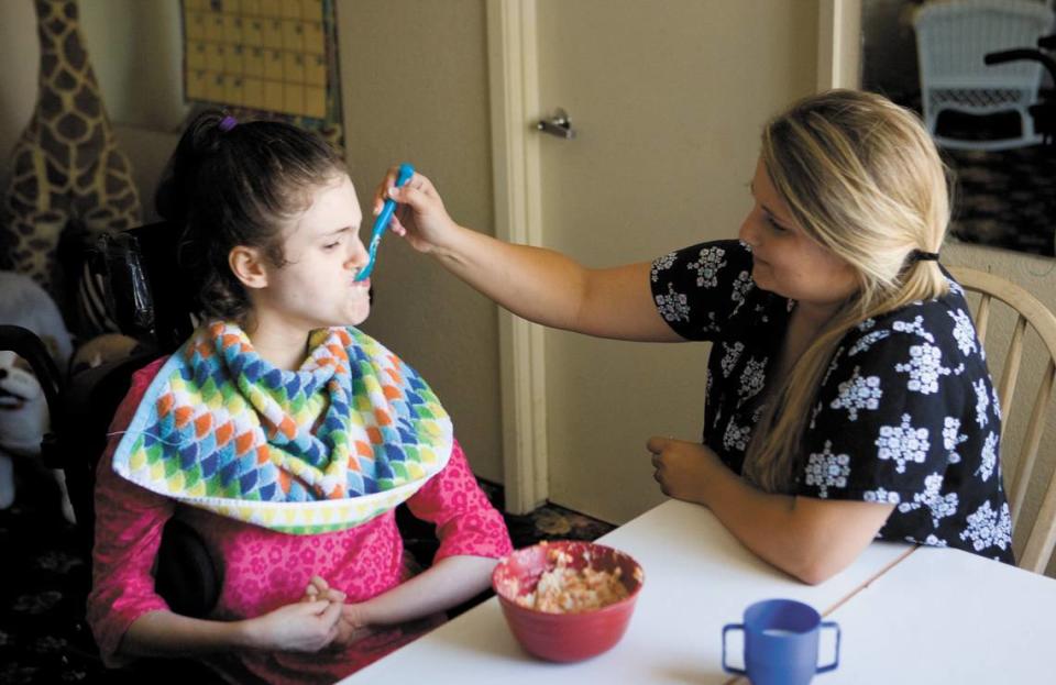 Blair Gracey, a certified nursing assistant, feeds Emonee, one of the children at Sjany de Groot’s former nursing home in San Luis Obispo.