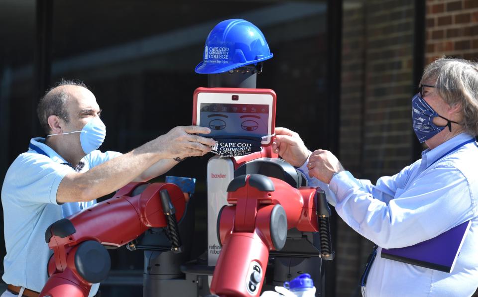 Rick Bsharah, left, and Bob Bartholomay rig up Baxter the robot with a COVID-19 mask before it went to work moving sand at the Cape Cod Community College campus in West Barnstable on Aug. 11, 2020. Community leaders and school officials held a groundbreaking ceremony for the new Frank and Maureen Wilkens Science and Engineering Center.